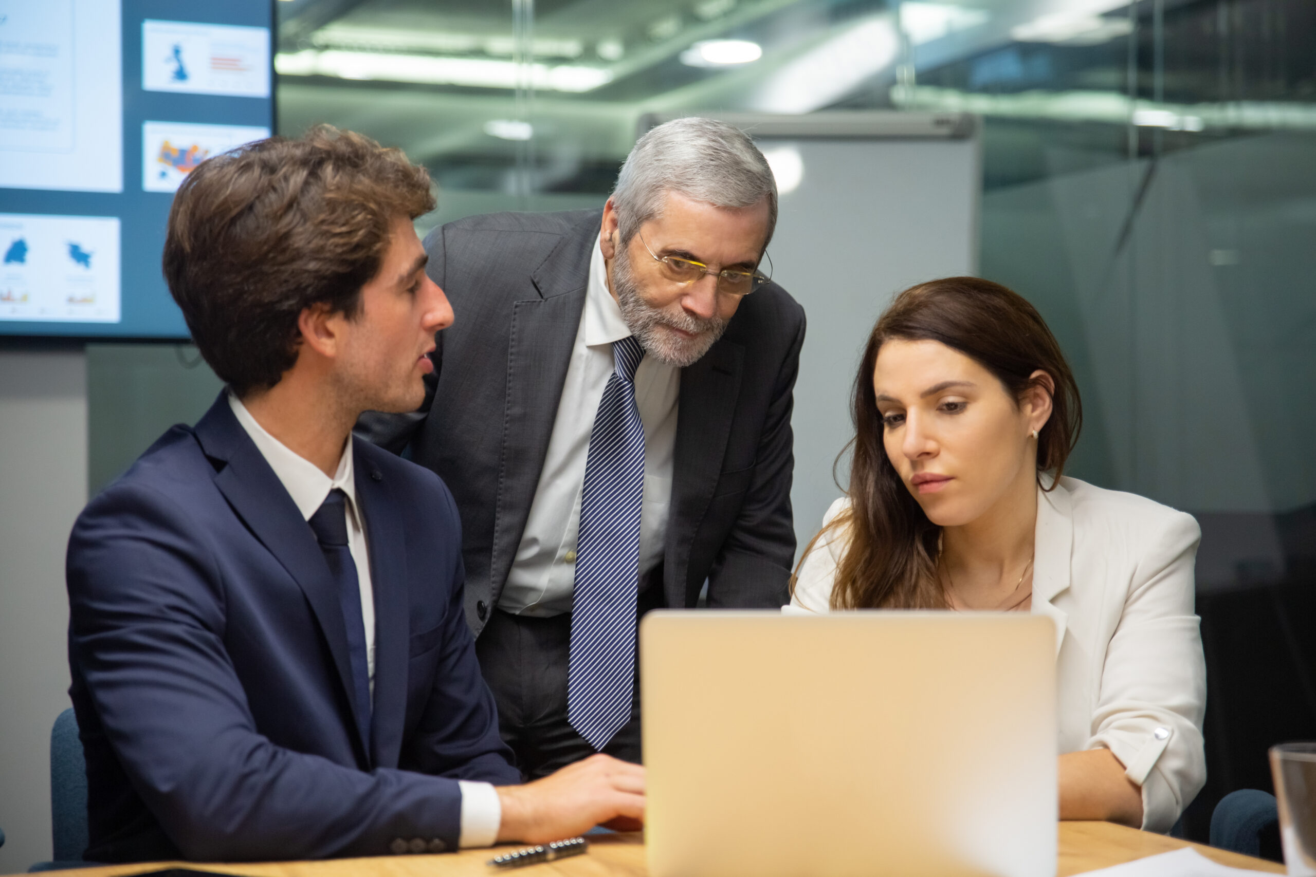Front view of confident business team looking at laptop. Group of office employees sitting at table and discussing new project. Business, teamwork concept